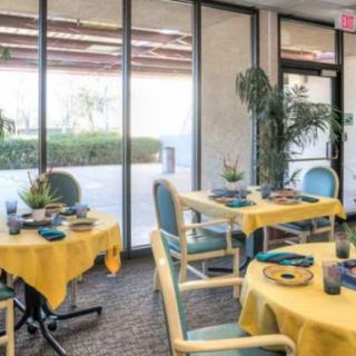 A cozy dining area with yellow tablecloths and large windows overlooking greenery.