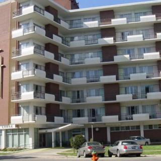 A multi-story residential apartment building with balconies and parked cars in front.