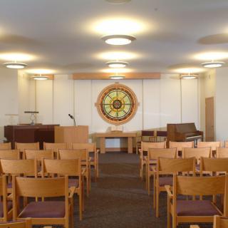 An interior view of a small chapel with wooden chairs and a stained glass window.