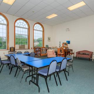 A spacious meeting room with blue tables, chairs, and large arched windows.