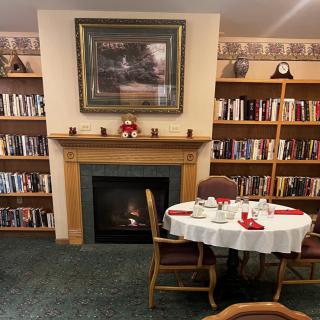 A cozy corner of a library featuring a fireplace surrounded by bookshelves and a set dining table.