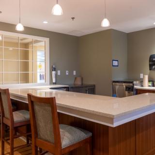 A modern kitchen interior with a dining area, featuring a countertop, chairs, and pendant lighting.