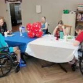 A group of people seated around a table with balloons indoors.