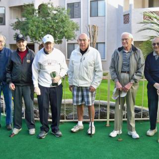 A group of senior men standing together with golf equipment on a green lawn.