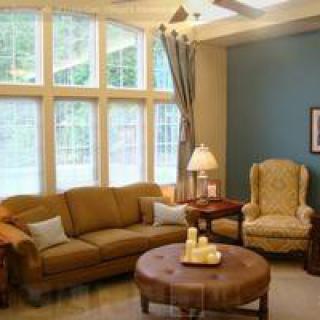 A cozy living room with a large sofa, elegant armchair, and ample natural light from the tall windows.