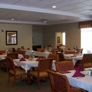 An empty dining room with neatly arranged tables and chairs, featuring white tablecloths and red napkins.