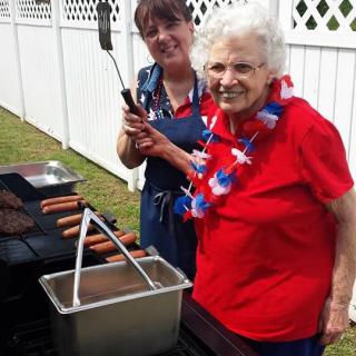 Two women enjoying a barbecue, grilling hot dogs outdoors during a summer celebration.