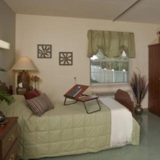 A cozy bedroom with a neatly made bed, decorative pillows, and a bedside lamp. The room features a window with curtains and tasteful decor.