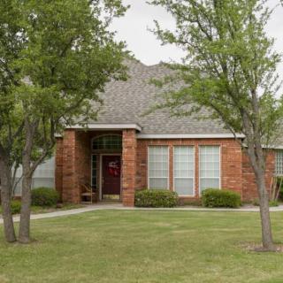 A brick house surrounded by trees and a well-kept lawn.