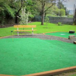 A serene mini golf course surrounded by lush greenery with a park bench in the background.