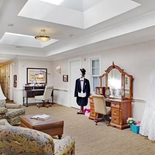 A spacious living room with comfortable seating and a decorative dressing table, featuring a mannequin dressed in formal attire.