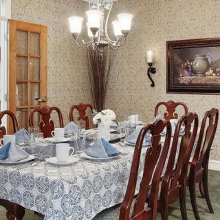 A well-decorated dining room with a full table setting, featuring elegant chairs and a chandelier.