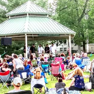 A lively outdoor concert taking place in a gazebo, with a large crowd enjoying the summer day.