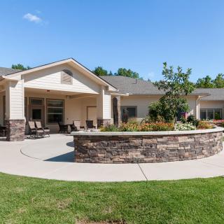 A modern residential building with a landscaped garden and patio area under a clear blue sky.