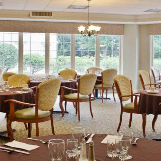 An elegant dining room with neatly set tables and comfortable chairs, featuring large windows that allow natural light to fill the space.