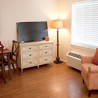 A cozy living room with a TV on a dresser, a lamp, and an armchair.