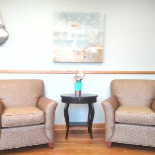 A cozy waiting area featuring two upholstered chairs, a small table with a drink, and an abstract painting on the wall.