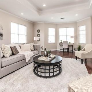 A bright and cozy living room with a neutral color scheme, featuring a comfortable sofa, round coffee table, armchair, and large windows that let in plenty of natural light.