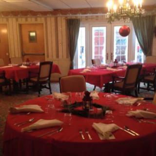 A warmly lit dining room with tables covered in red tablecloths and surrounded by chairs.