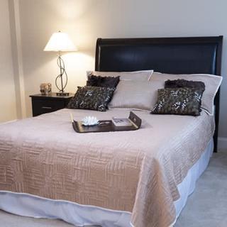 A neatly made bed with a beige quilt and decorative pillows in a cozy bedroom setting.