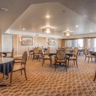 An elegantly decorated dining room with round tables and upholstered chairs on a patterned carpet.