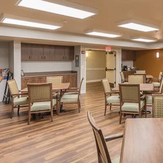 A spacious dining area with wooden flooring and neatly arranged tables and chairs.