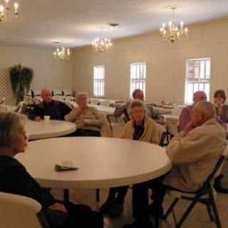 A group of seniors gathered at round tables in a well-lit room.