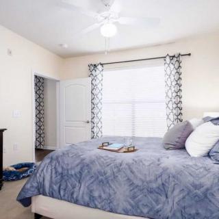 A cozy bedroom with a neatly made bed, patterned curtains, and a ceiling fan.