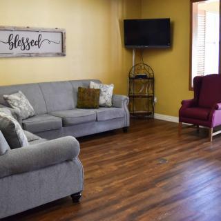A cozy living room with gray sofas, a burgundy armchair, and a wall-mounted television.
