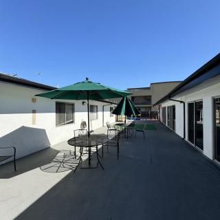 A sunny outdoor patio area with tables, chairs, and umbrellas between buildings.