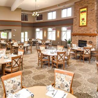 A spacious and elegantly furnished dining area featuring round tables, cushioned chairs, and a cozy fireplace.
