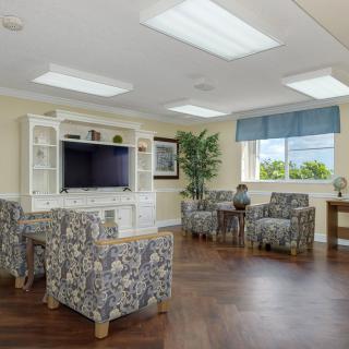 A cozy living room with patterned chairs, a large television, and natural lighting from a window.