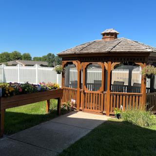 A charming wooden gazebo surrounded by greenery on a sunny day.