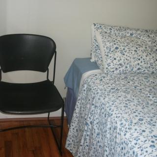 A simple bedroom setup with a chair next to a bed covered in patterned bedding.