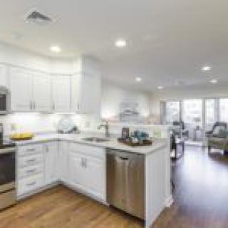 A modern kitchen with white cabinets and stainless steel appliances, featuring an open space layout with hardwood flooring.