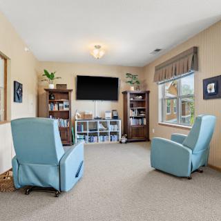 A cozy living room featuring two comfortable blue chairs and a television, complemented by bookshelves and decorative plants.