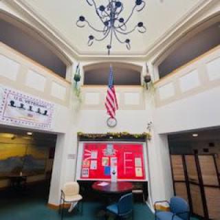 A modern lobby area featuring a chandelier, a red display board, and an American flag.