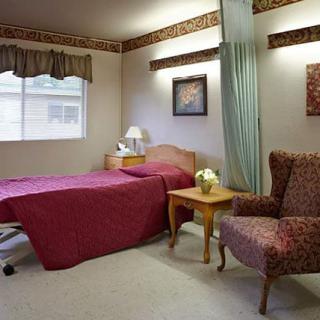 A hospital room with a single bed, a chair, and a bedside table.