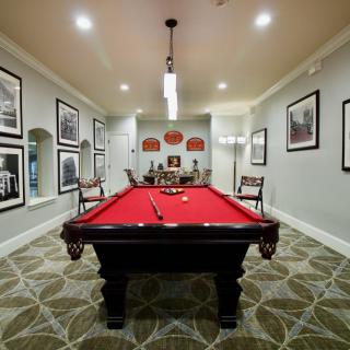 A stylish game room featuring a red-felt billiards table, surrounded by framed artwork and elegant decor.