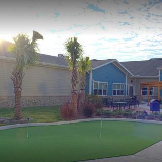 A sunny view of a building with palm trees and a putting green in the foreground.
