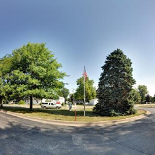 A serene park scene featuring lush green trees and a flag, under a clear blue sky.