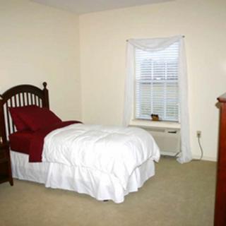 A simple bedroom with a single bed and white bedding next to a window.