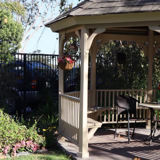 A charming gazebo in a sunlit garden with a wooden bench and hanging flower basket.