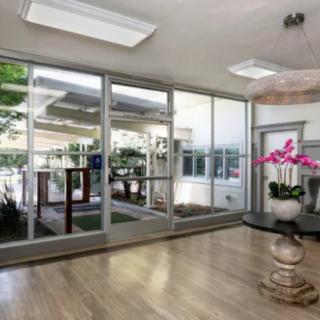 A modern lobby with large glass walls, wooden flooring, and decorative plants, allowing for ample natural light.