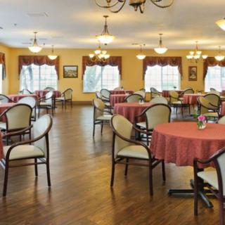 A spacious dining area with multiple tables and chairs, featuring chandeliers and wooden flooring.