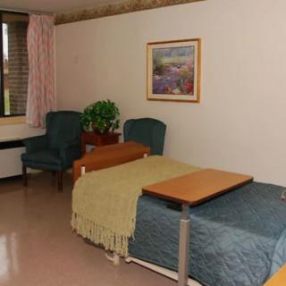 A hospital room with two beds, chairs, a window, and decor like a plant and painting.