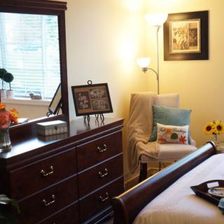 A cozy bedroom interior with a dresser, chair, and soft lighting.