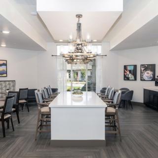 A modern dining room featuring a long table with chairs and a central chandelier.