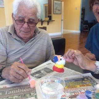 An elderly man participating in a craft activity, painting a small figurine with colorful paints.
