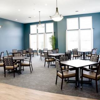 A modern dining area with multiple tables and chairs, illuminated by large windows and stylish ceiling lights.